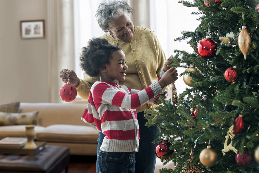 Grandmother and grandchild hanging ornaments on a Christmas tree.