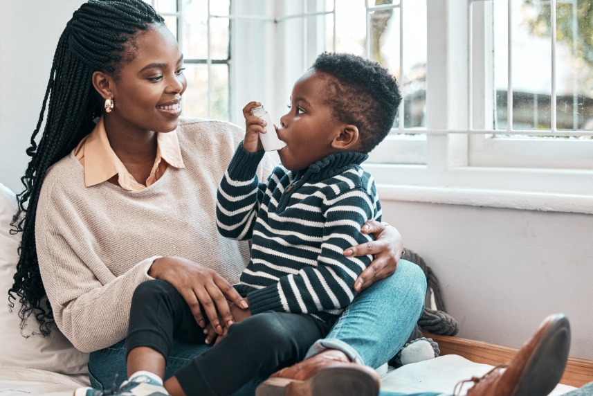 A woman holds her toddler son and teaches him to use his inhaler to manage his asthma.