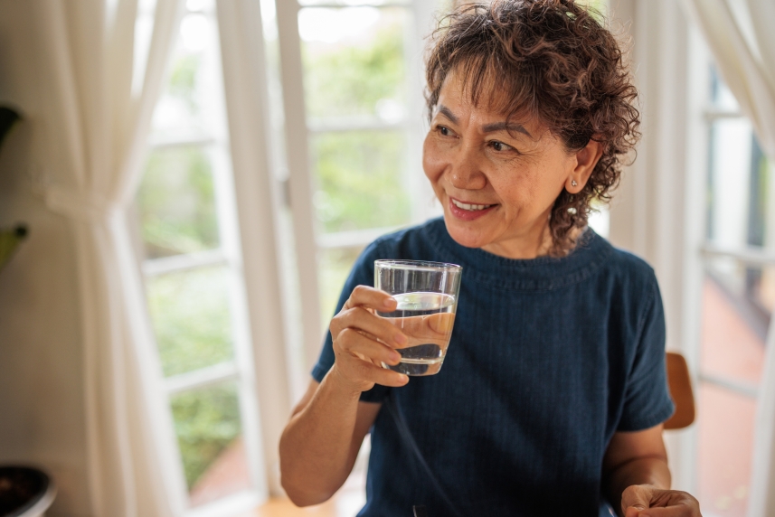 A woman smiles as she prepares to take a sip of water from a glass she's holding.