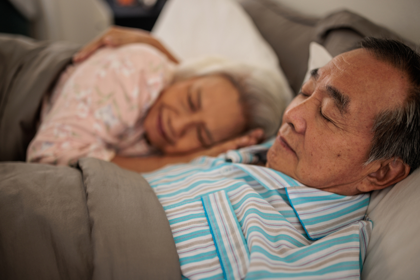 A man and woman sleep side-by-side in bed.