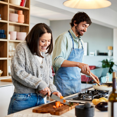 A man and woman smiling, cooking in a kitchen together