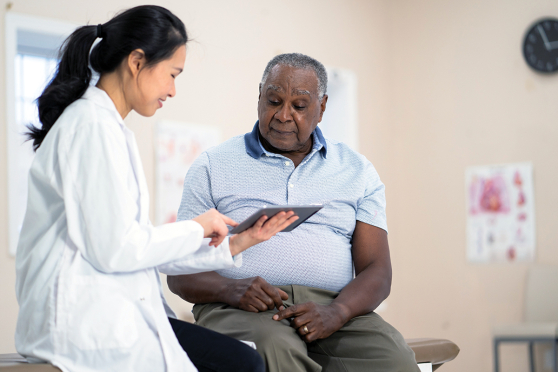 A man sits on an exam table and talks with his doctor