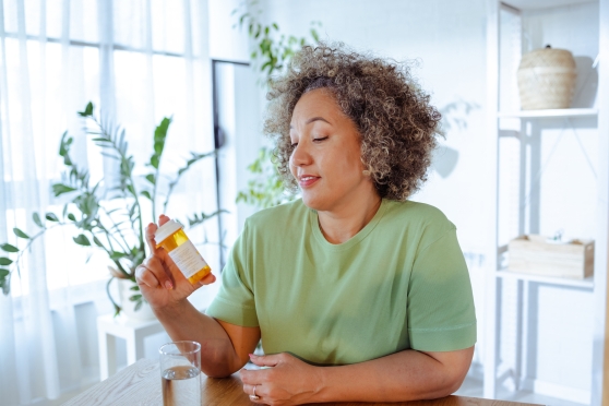 A woman in a green T-shirt reads her prescription label on an orange pill bottle.