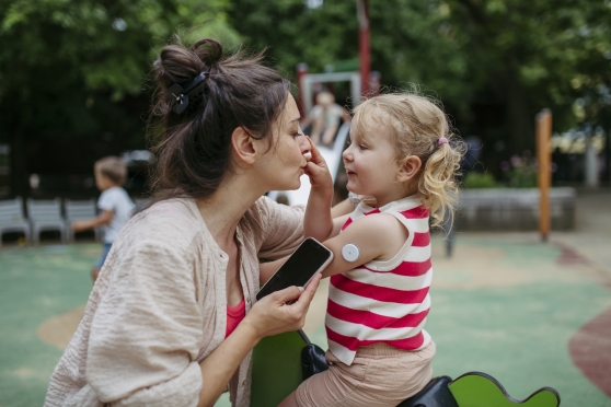 A woman helps her toddler daughter check her blood sugar levels using a continuous glucose monitor.