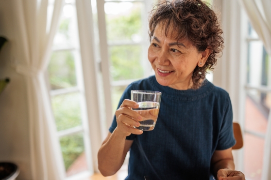 A woman smiles as she prepares to take a sip of water from a glass she's holding.