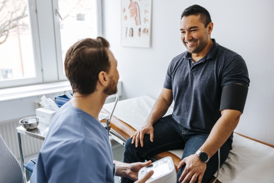 A man smiled at his doctor while he sits on the exam table.